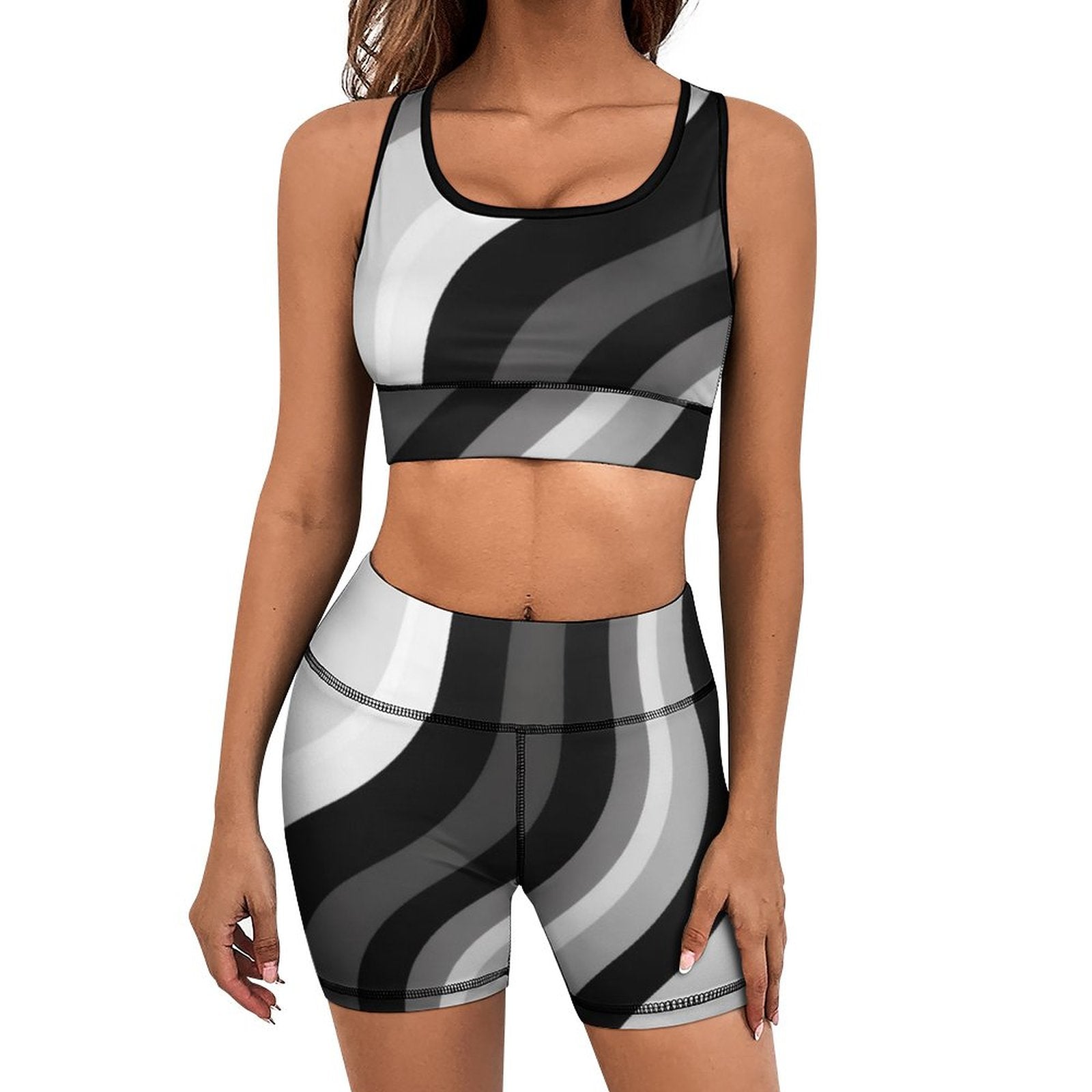A woman modeling a matching activewear set with a sports bra and high-waisted biker shorts featuring a wavy black, gray, and white striped pattern, set against a plain white background.